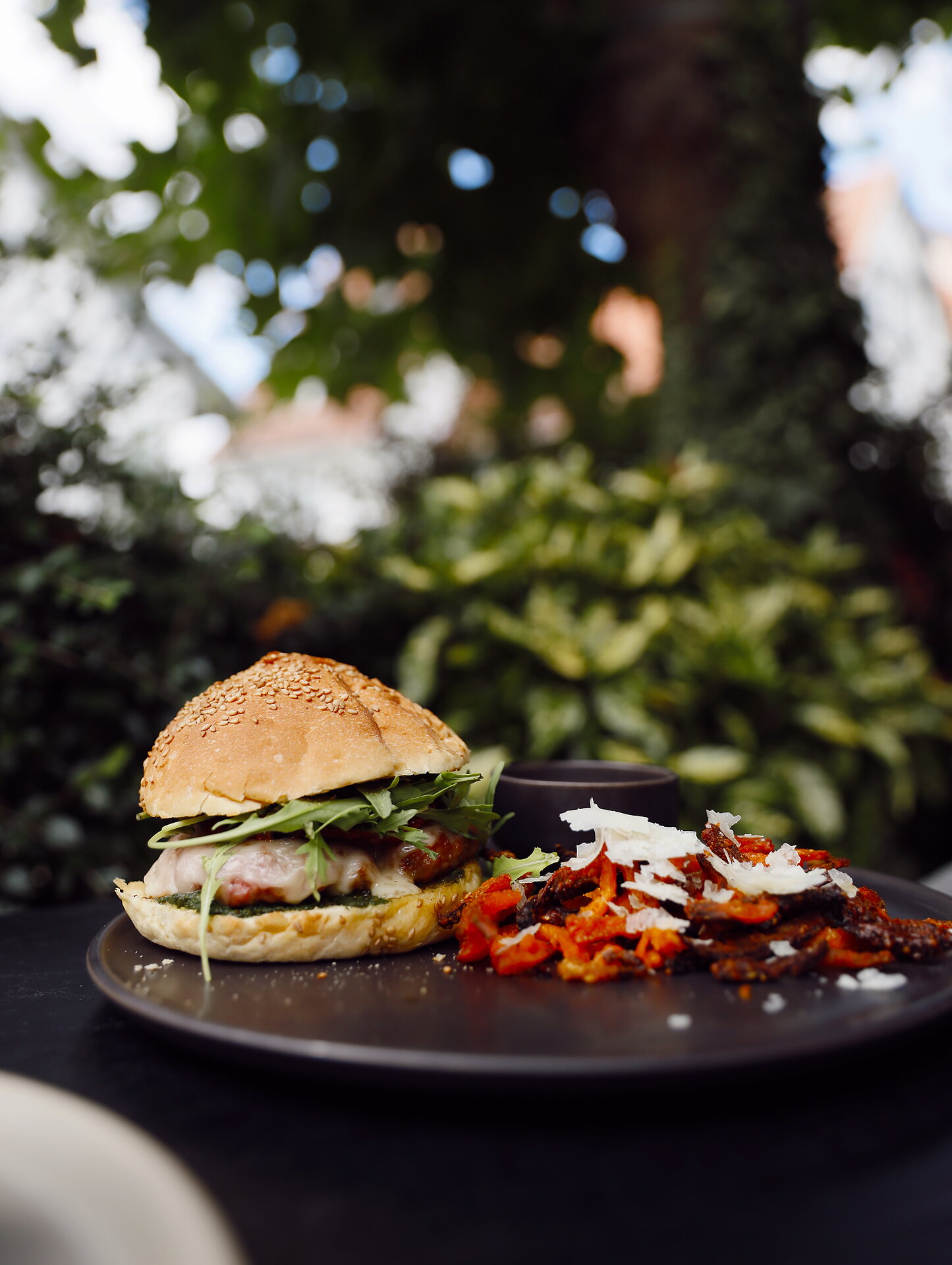 Ein Hamburger mit Salat und Käse auf einem Teller, daneben ein Gericht mit Tomaten und Käse.
